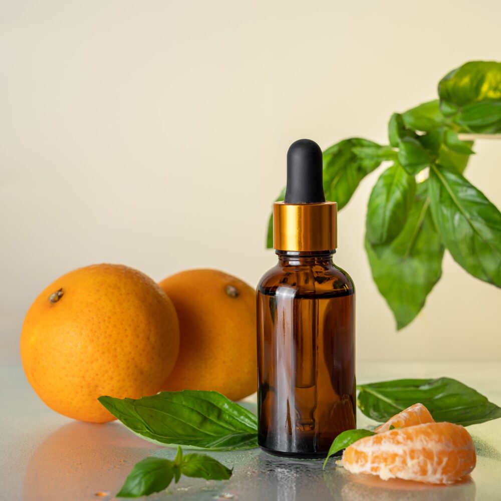 Glass brown bottle with serum and tangerines with basil for skin care on a light background